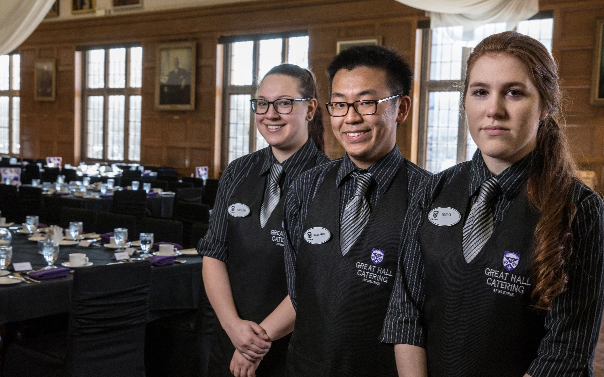 Three catering staff in uniform, standing next to each other, smiling at the camera.